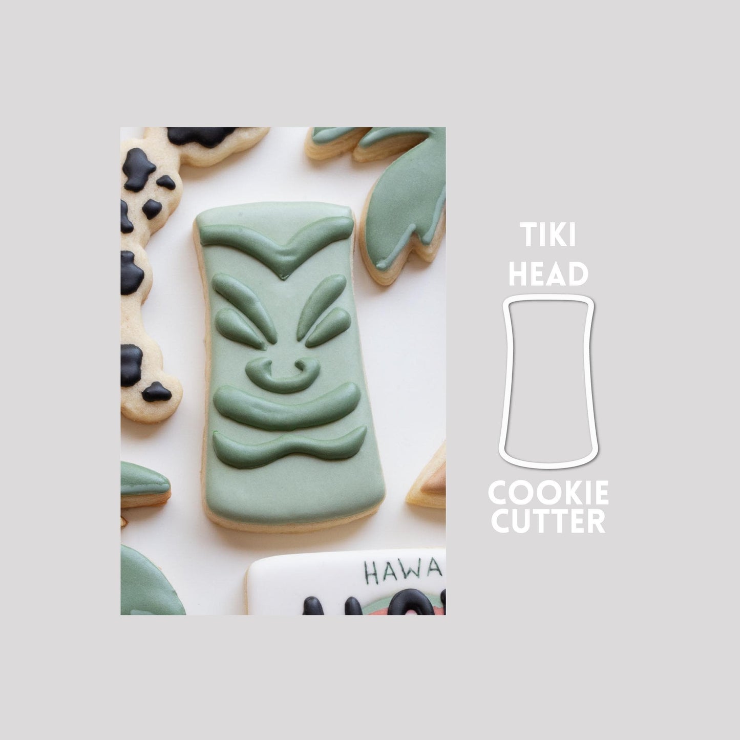 Decorated tiki head sugar cookie next to a tiki head cookie cutter outline on a gray background.
