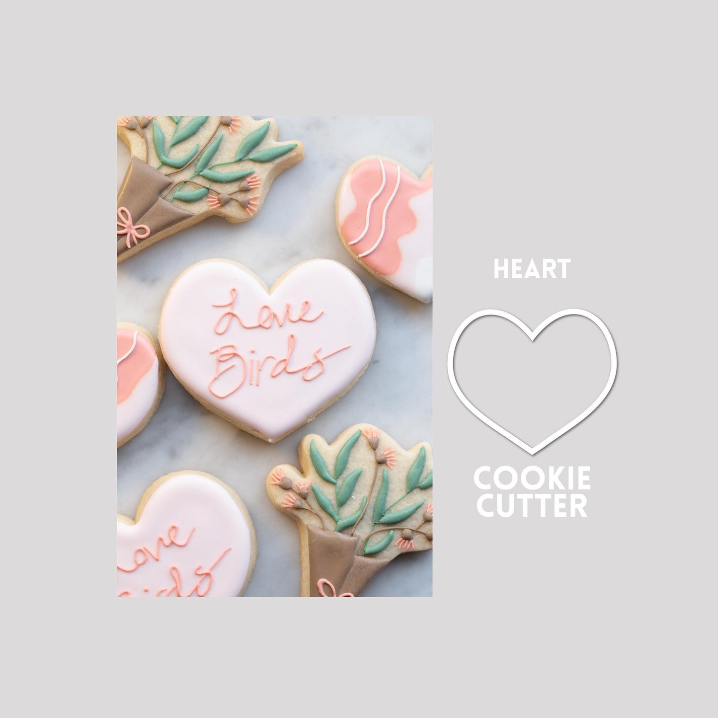 Decorated heart sugar cookie next to a heart cookie cutter outline on a gray background.