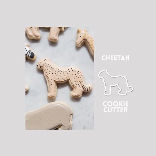 Decorated cheetah sugar cookie next to a cheetah cookie cutter outline on a gray background.