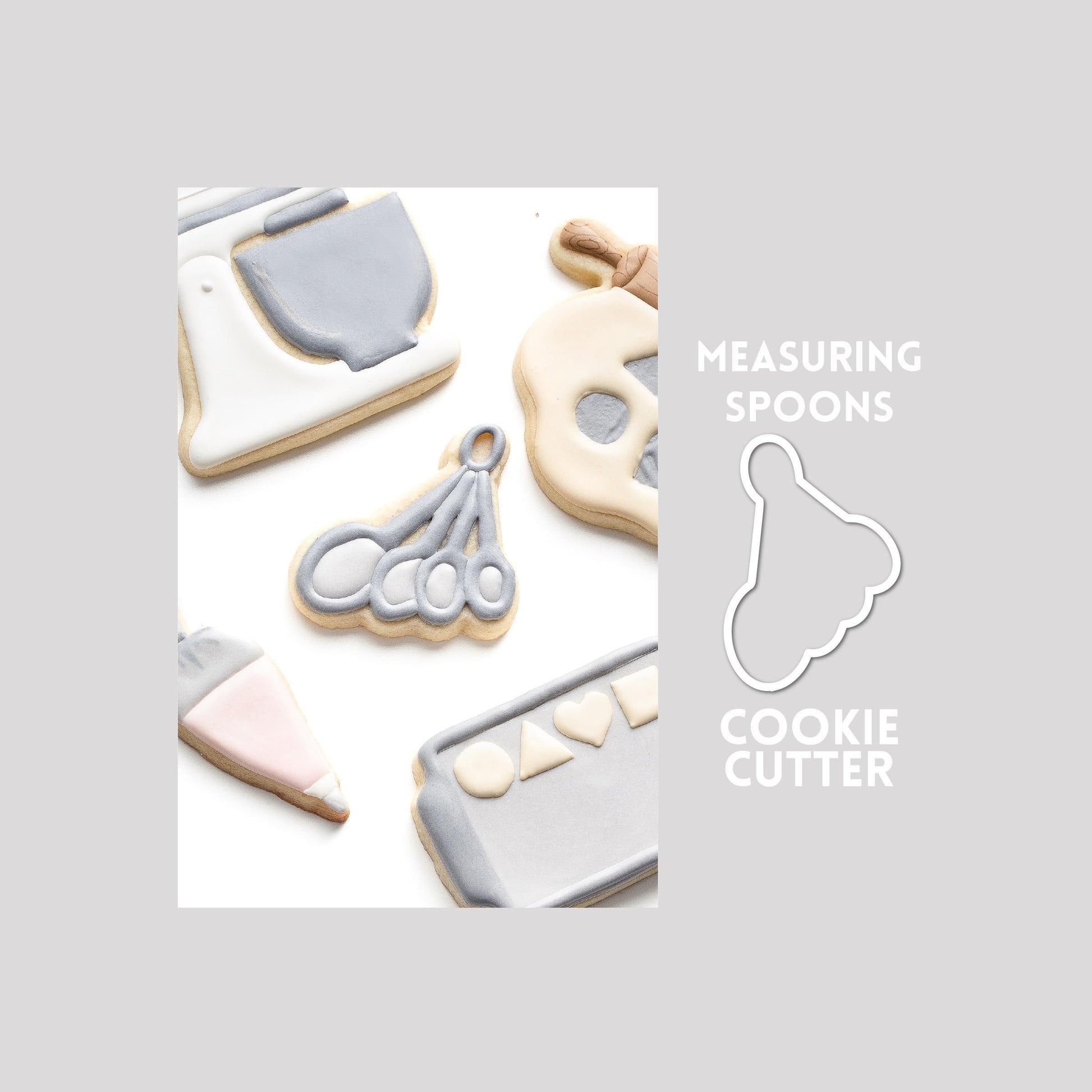 Decorated measuring spoons sugar cookie next to a measuring spoons cookie cutter outline on a gray background.