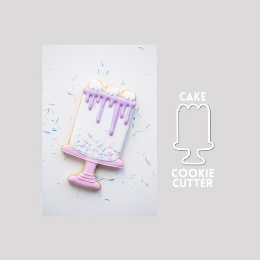 Decorated cake sugar cookie next to a cake cookie cutter outline on a gray background.