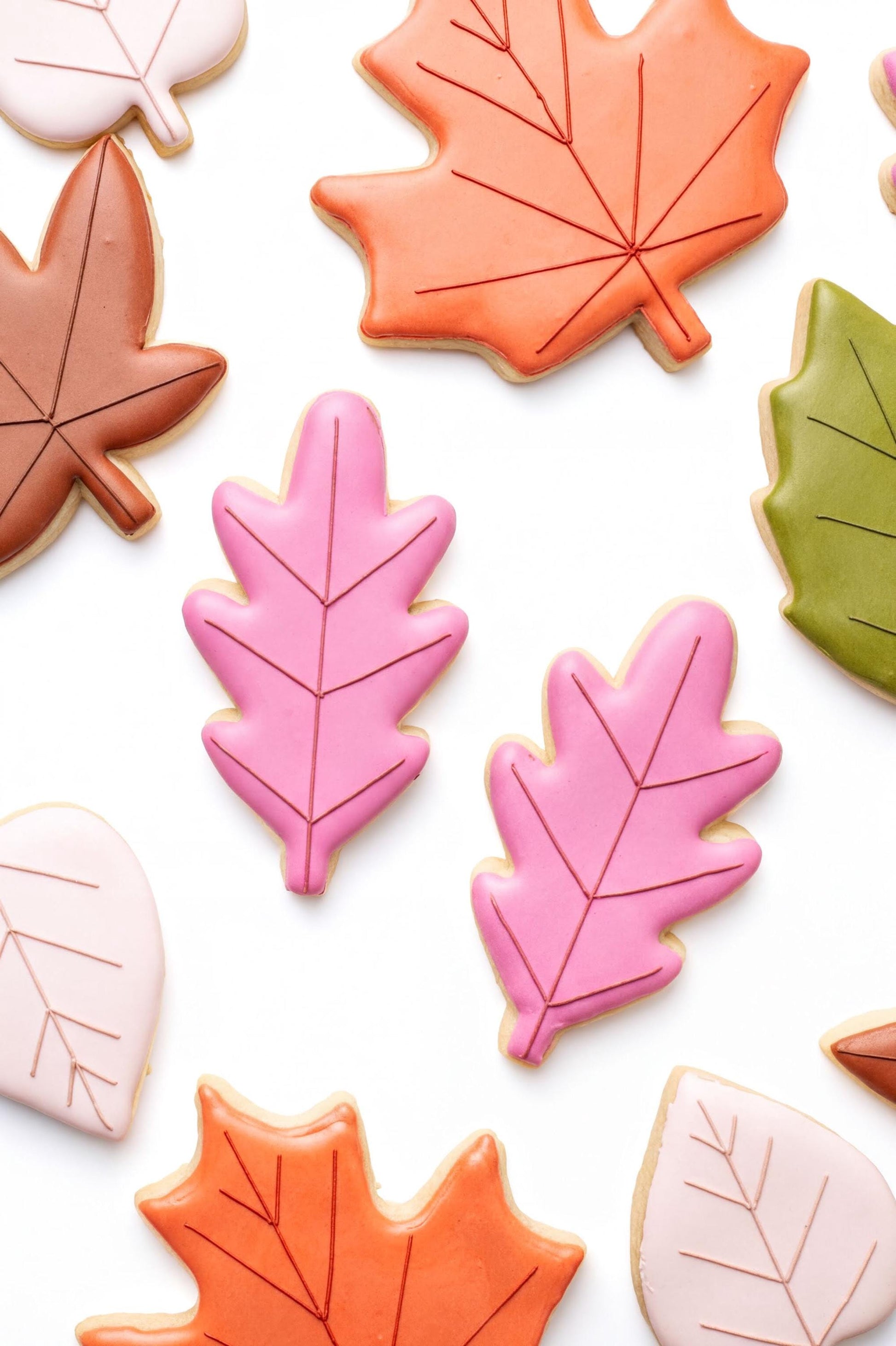 a variety of colorful and decorated cookies shaped like leaves, including maple leaves and autumn leaves in shades of pink, orange, and green.