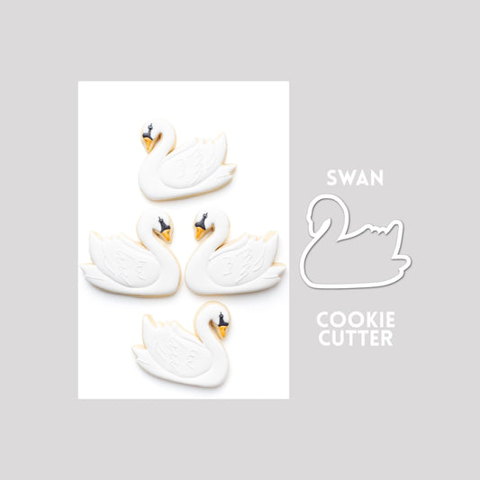 Decorated swan sugar cookie next to a swan cookie cutter outline on a gray background.