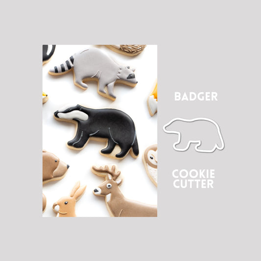 Decorated badger sugar cookie next to a badger cookie cutter outline on a gray background.