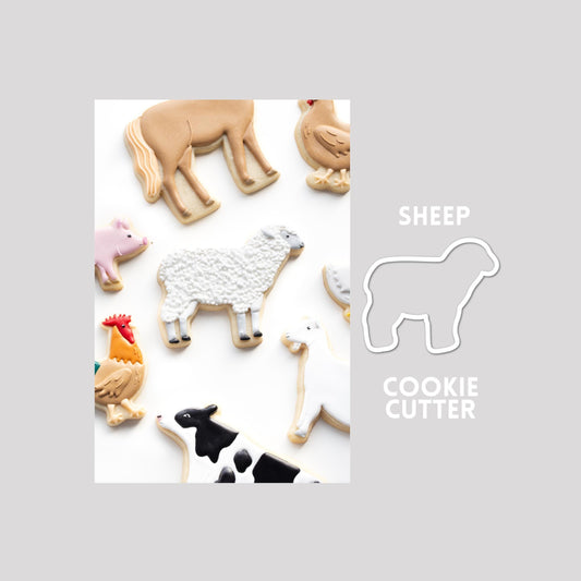 Decorated sheep sugar cookie next to a sheep cookie cutter outline on a gray background.