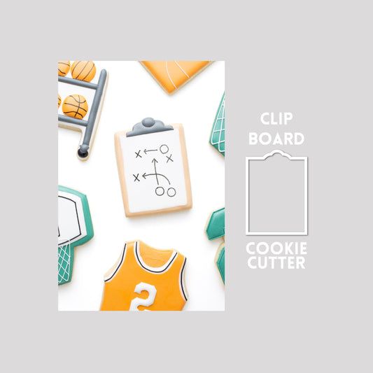 Decorated clipboard sugar cookie next to a clipboard cookie cutter outline on a gray background.