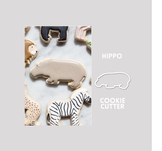 Decorated hippo sugar cookie next to a hippo cookie cutter outline on a gray background.