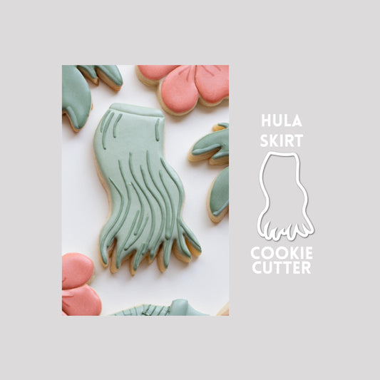 Decorated hula skirt sugar cookie next to a hula skirt cookie cutter outline on a gray background.