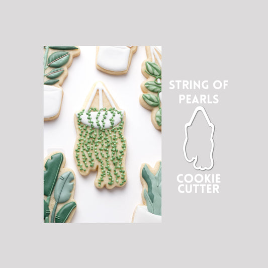 Decorated string of pearls plant sugar cookie next to a string of pearls plant cookie cutter outline on a gray background.