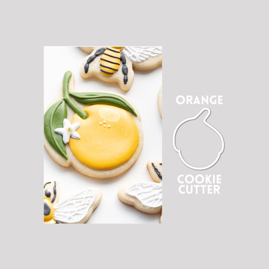 Decorated orange with stem sugar cookie next to a orange cookie cutter outline on a gray background.