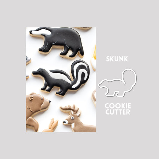 Decorated skunk sugar cookie next to a skunk cookie cutter outline on a gray background.