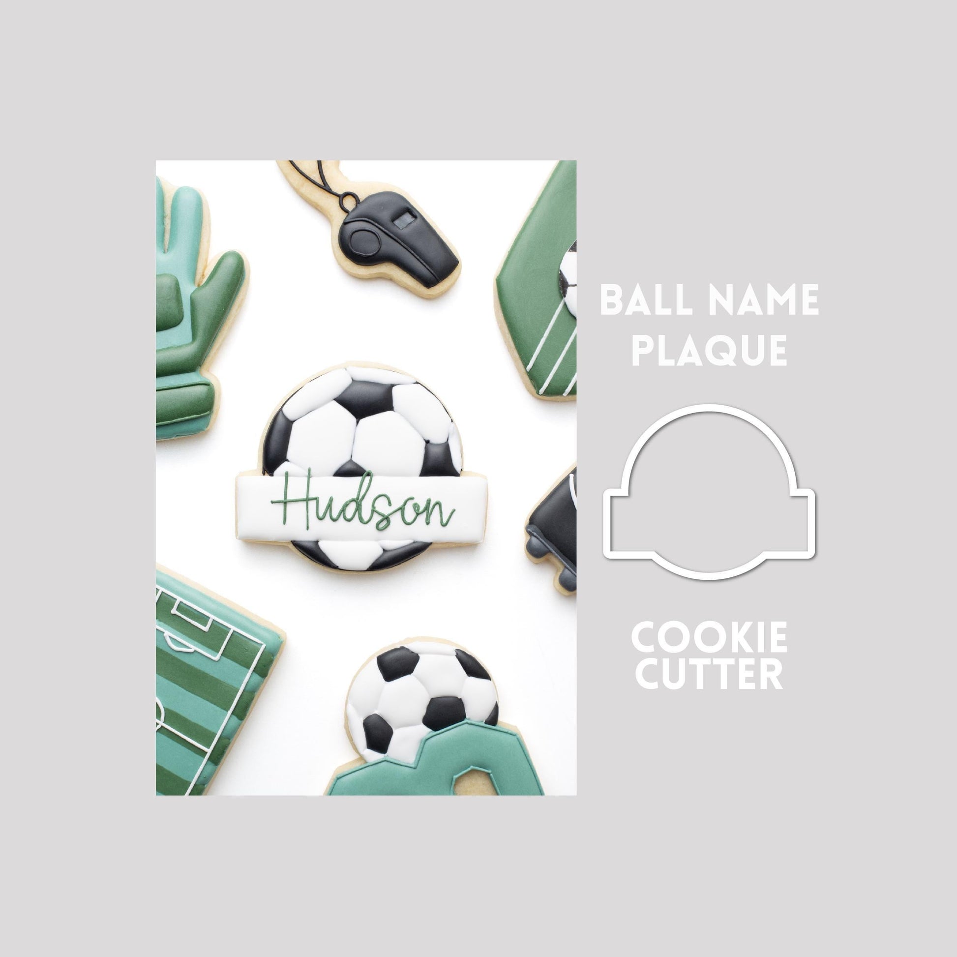 Decorated ball with name plaque sugar cookie next to a ball with name plaque cookie cutter outline on a gray background.