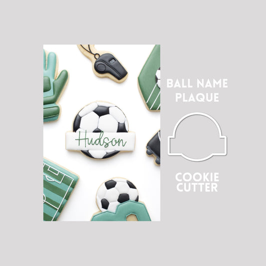 Decorated ball with name plaque sugar cookie next to a ball with name plaque cookie cutter outline on a gray background.