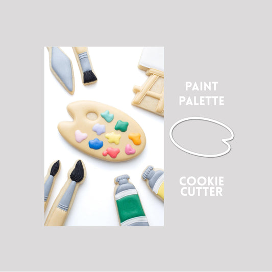 Decorated paint palette sugar cookie next to a paint palette cookie cutter outline on a gray background.