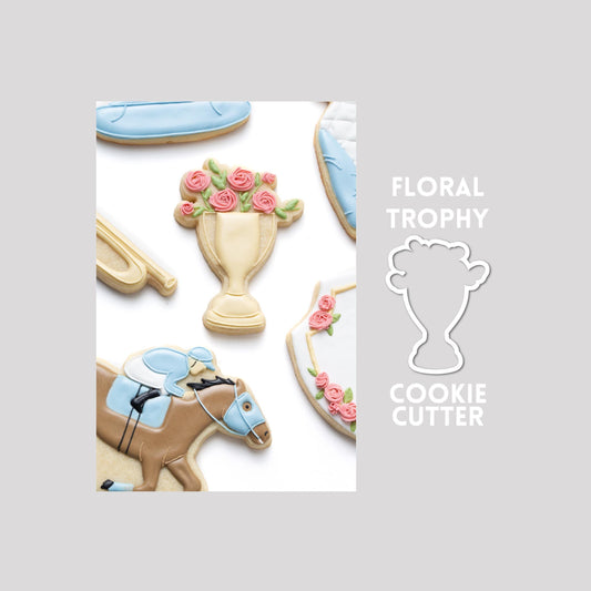 Decorated floral trophy sugar cookie next to a floral trophy cookie cutter outline on a gray background.