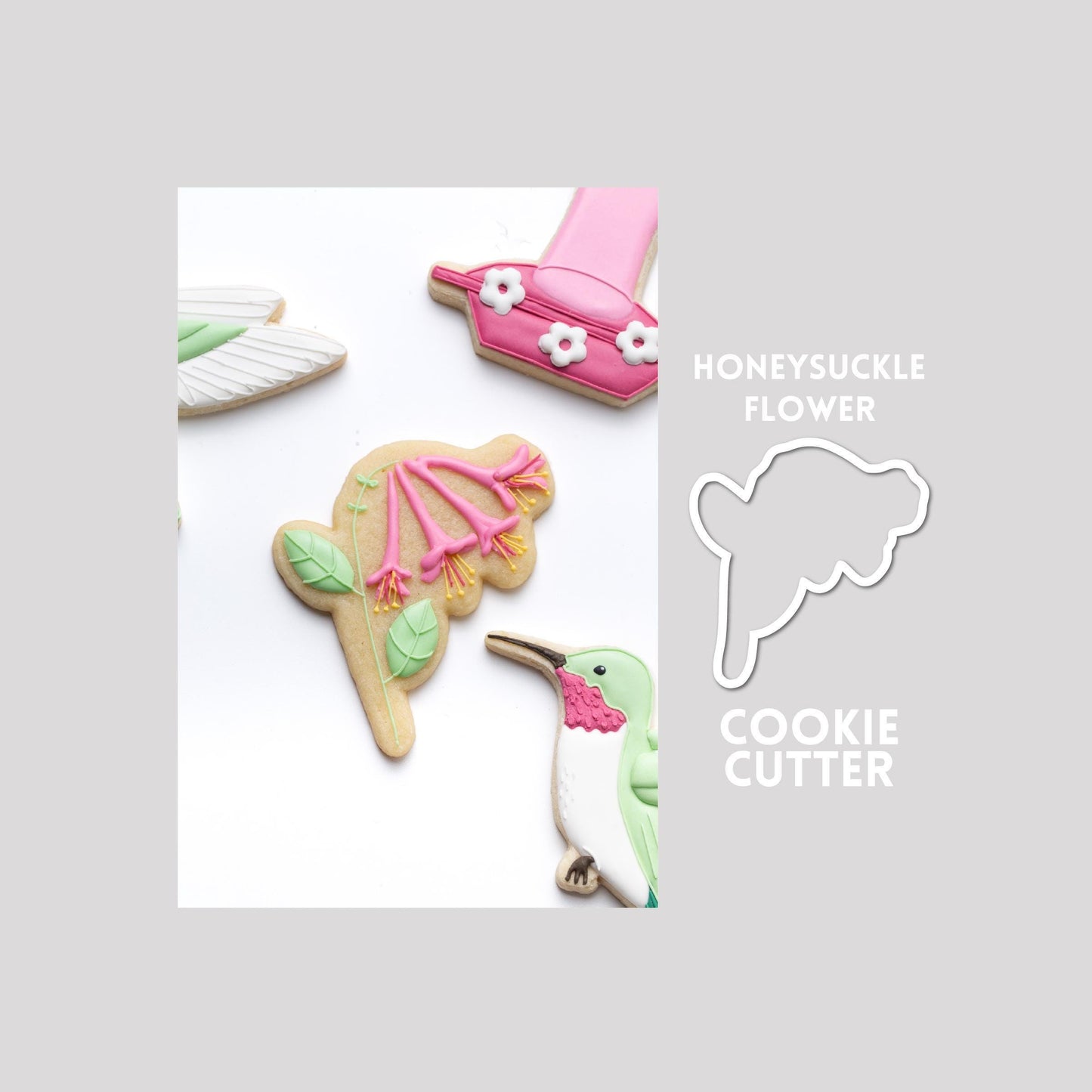 Decorated honeysuckle sugar cookie next to a honeysuckle cookie cutter outline on a gray background.