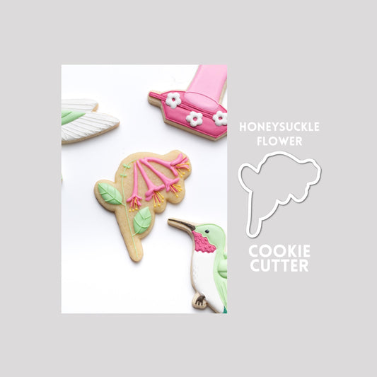 Decorated honeysuckle sugar cookie next to a honeysuckle cookie cutter outline on a gray background.