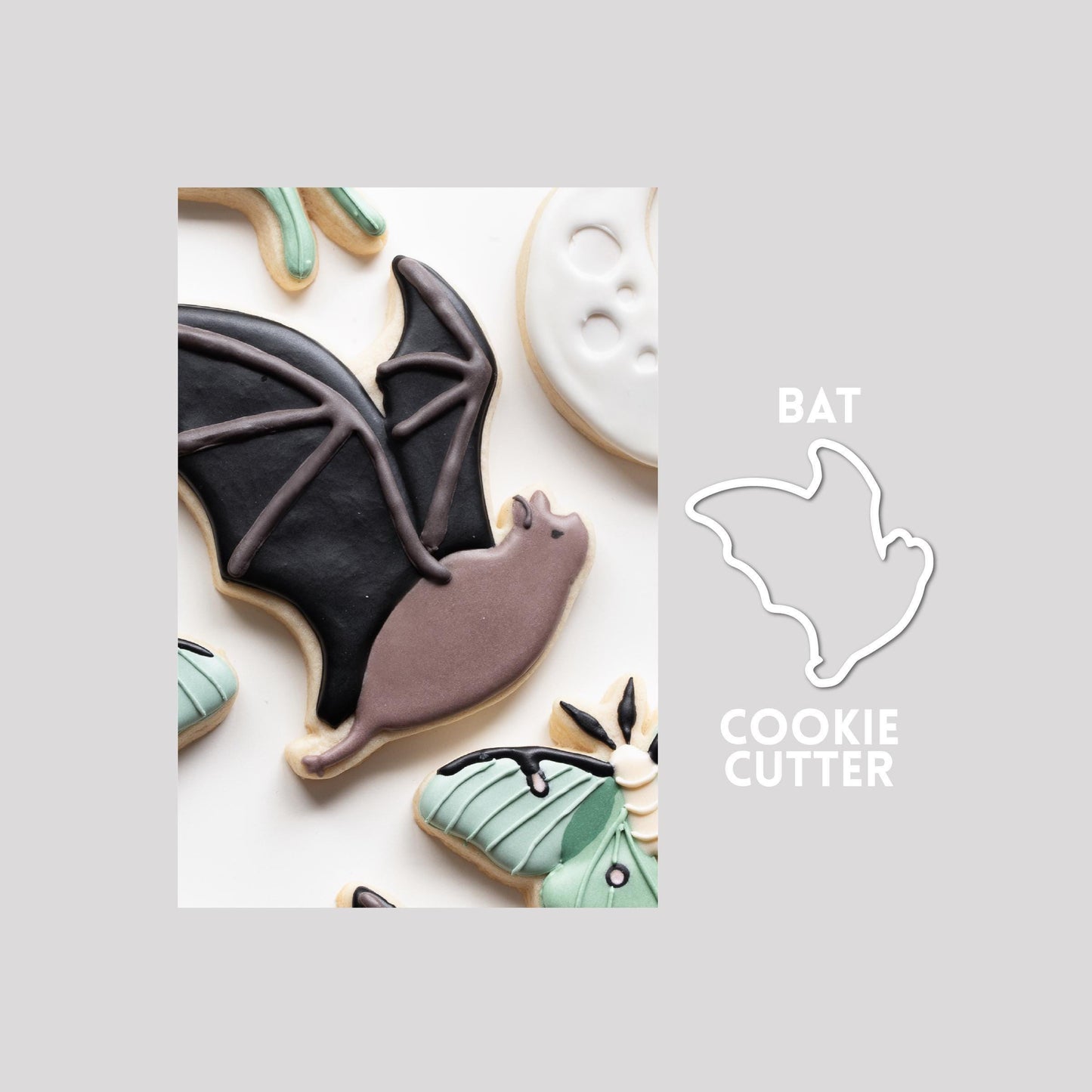 Decorated bat sugar cookie next to a bat cookie cutter outline on a gray background.