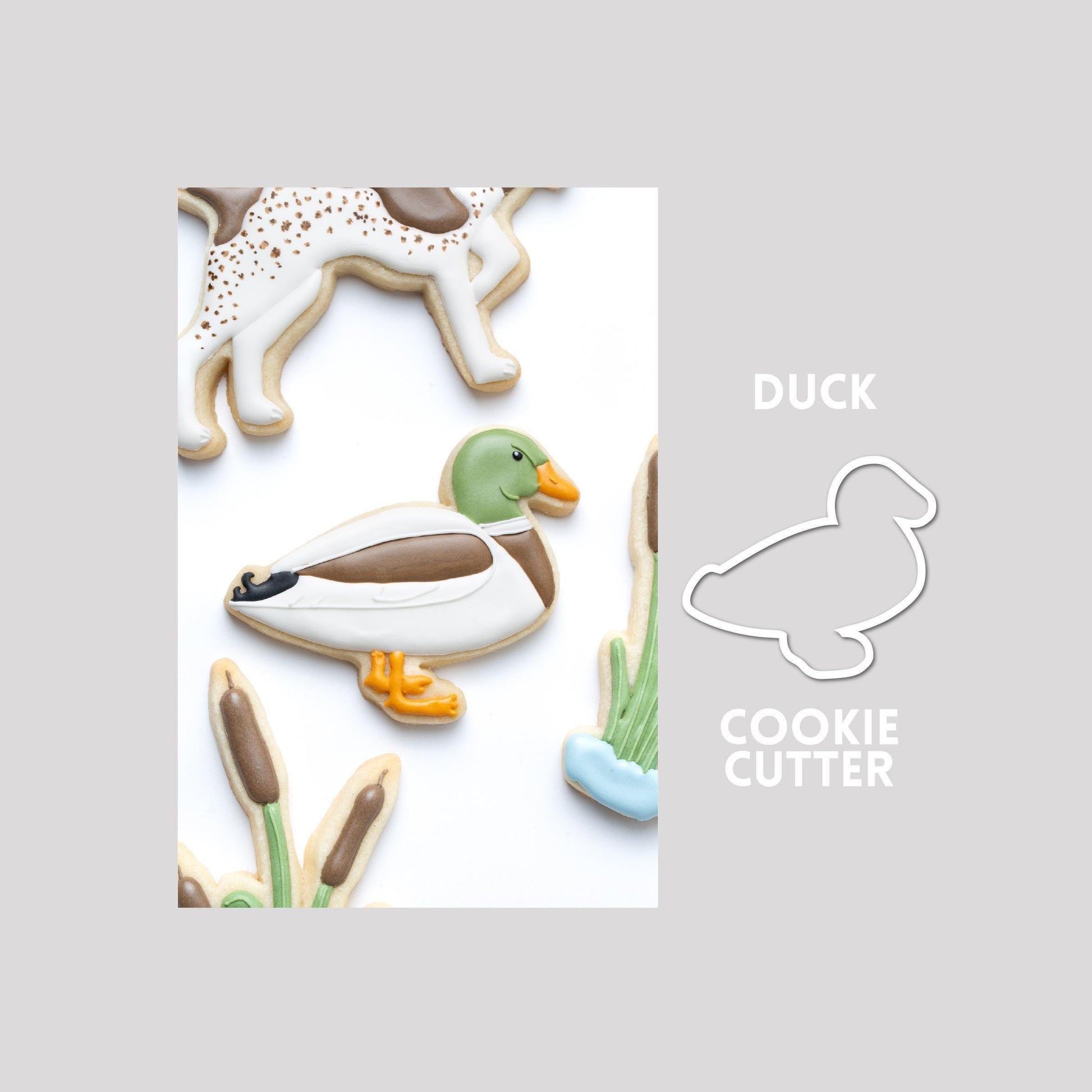 Decorated duck sugar cookie next to a duck cookie cutter outline on a gray background.