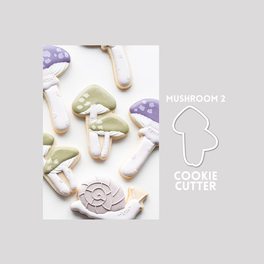 Decorated mushroom sugar cookie next to a mushroom cookie cutter outline on a gray background.