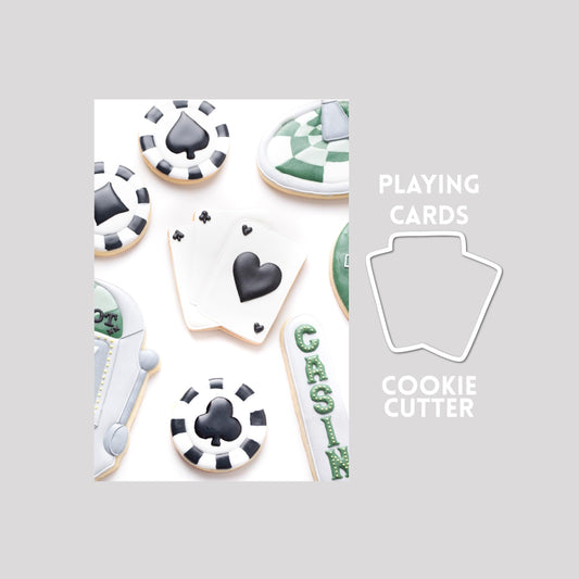 Decorated playing cards sugar cookie next to a playing cards cookie cutter outline on a gray background.