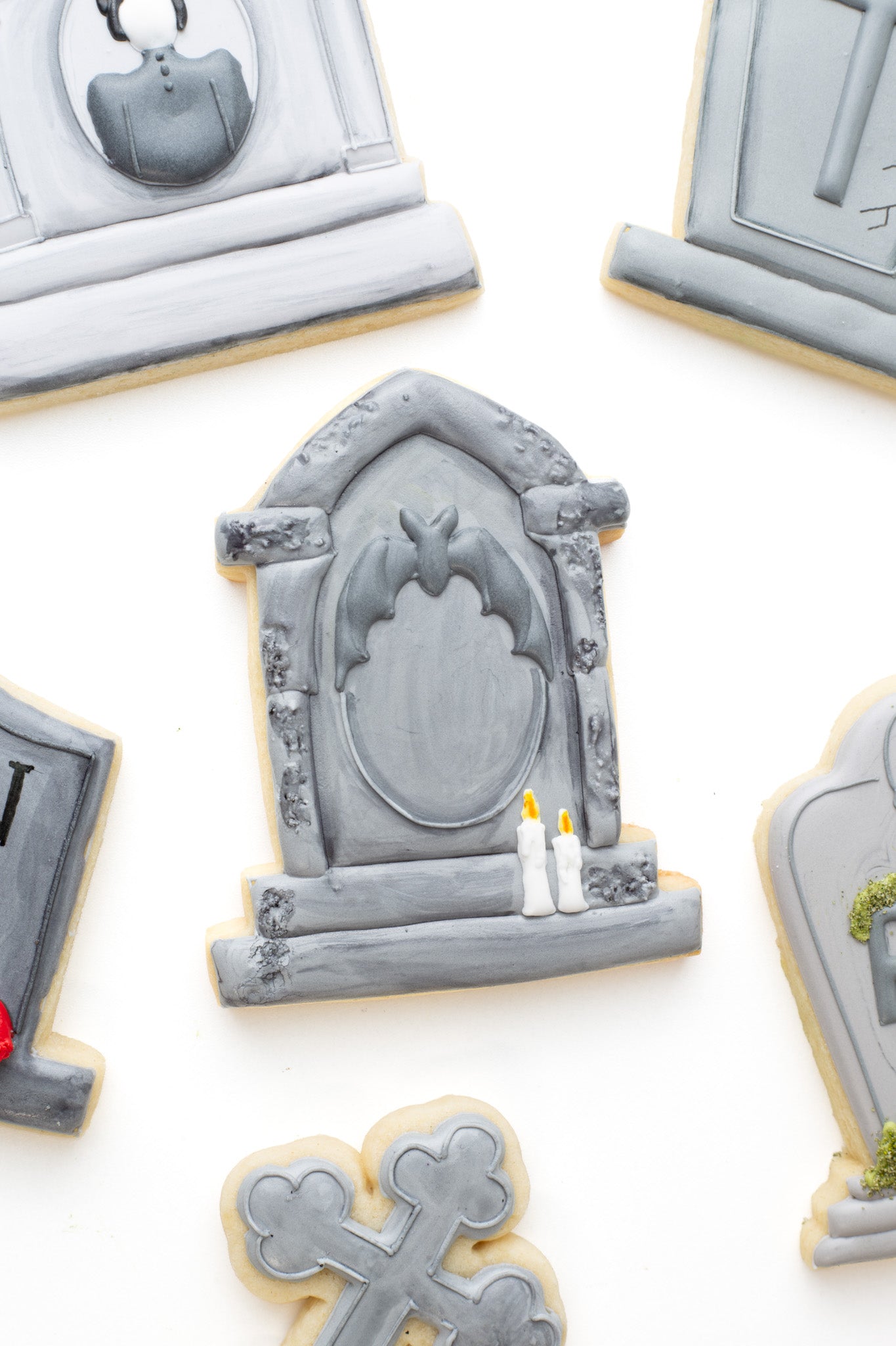 Decorated gravestone sugar cookies with a bat, and candles surrounded by other gravestones. 