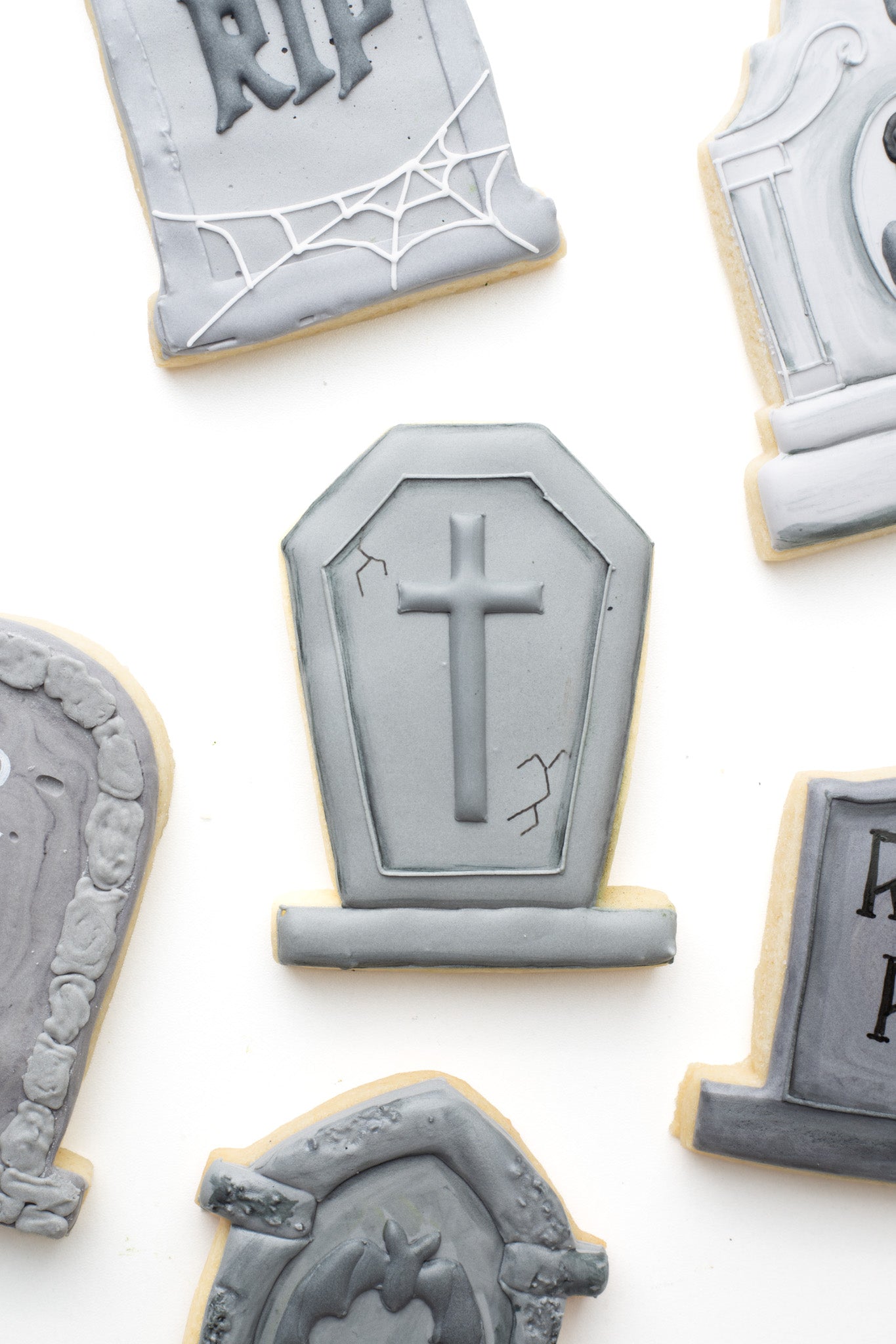 Gravestone decorated sugar cookie with a cross surrounded by other decorated sugar cookies. 