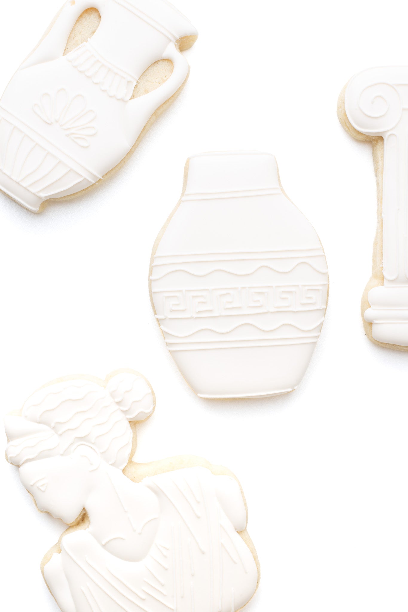 A greek vase decorated sugar cookie next to a greek statue and greek pillar.