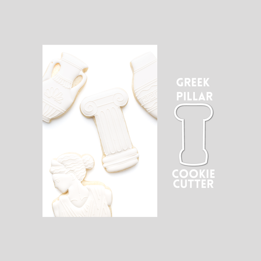 Decorated greek pillar sugar cookie next to a greek pillar cookie cutter outline on a gray background.