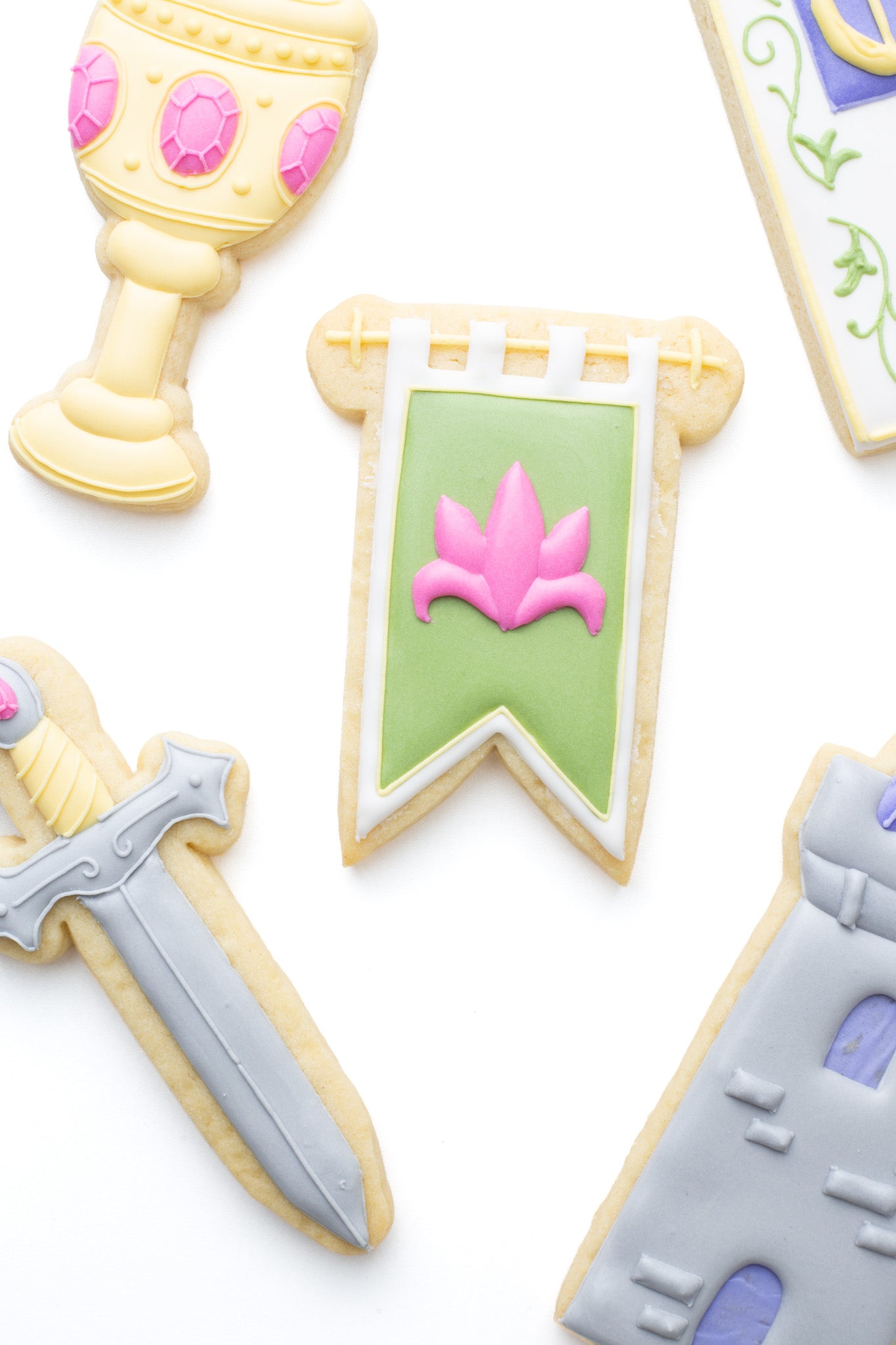 Medieval hanging banner decorated sugar cookie surrounded by a goblet, sword, castle tower and medieval manuscript  titled “Olivia’s Last Knight”.
