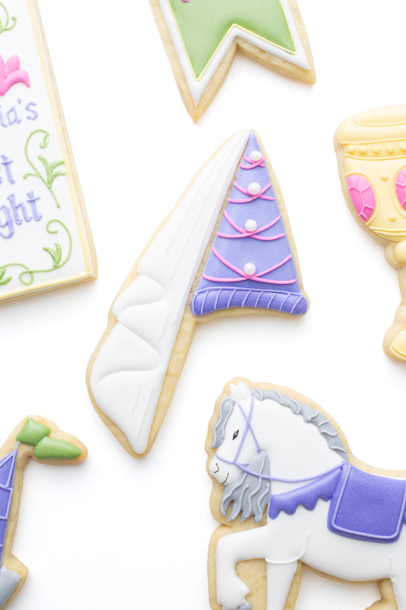 Princess hat decorated sugar cookie next to a horse, goblet, medieval banner, castle tower, and medieval manuscript titled “Olivia’s Last Knight”.
