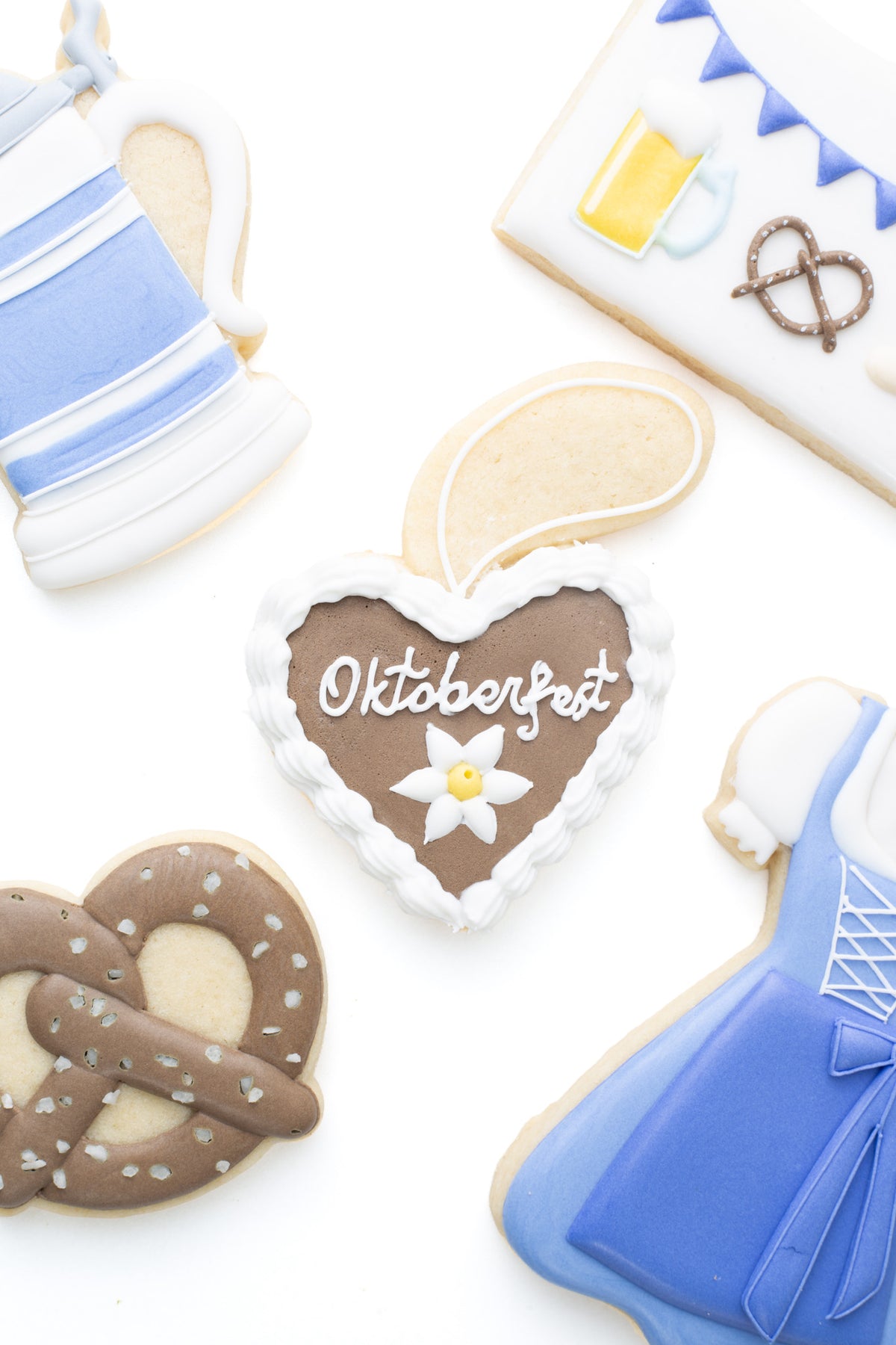 Oktoberfest themed cookies. Lebkuchen decorated sugar cookie next to a pretzel, beer stein, and dirndl dress decorated sugar cookie.