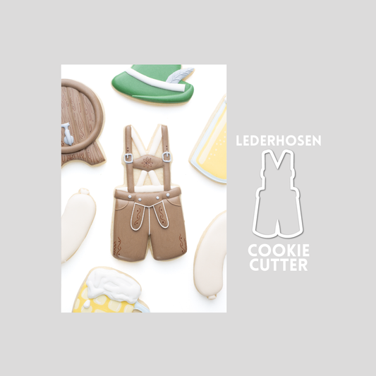 Decorated lederhosen sugar cookie next to a lederhosen cookie cutter outline on a gray background.