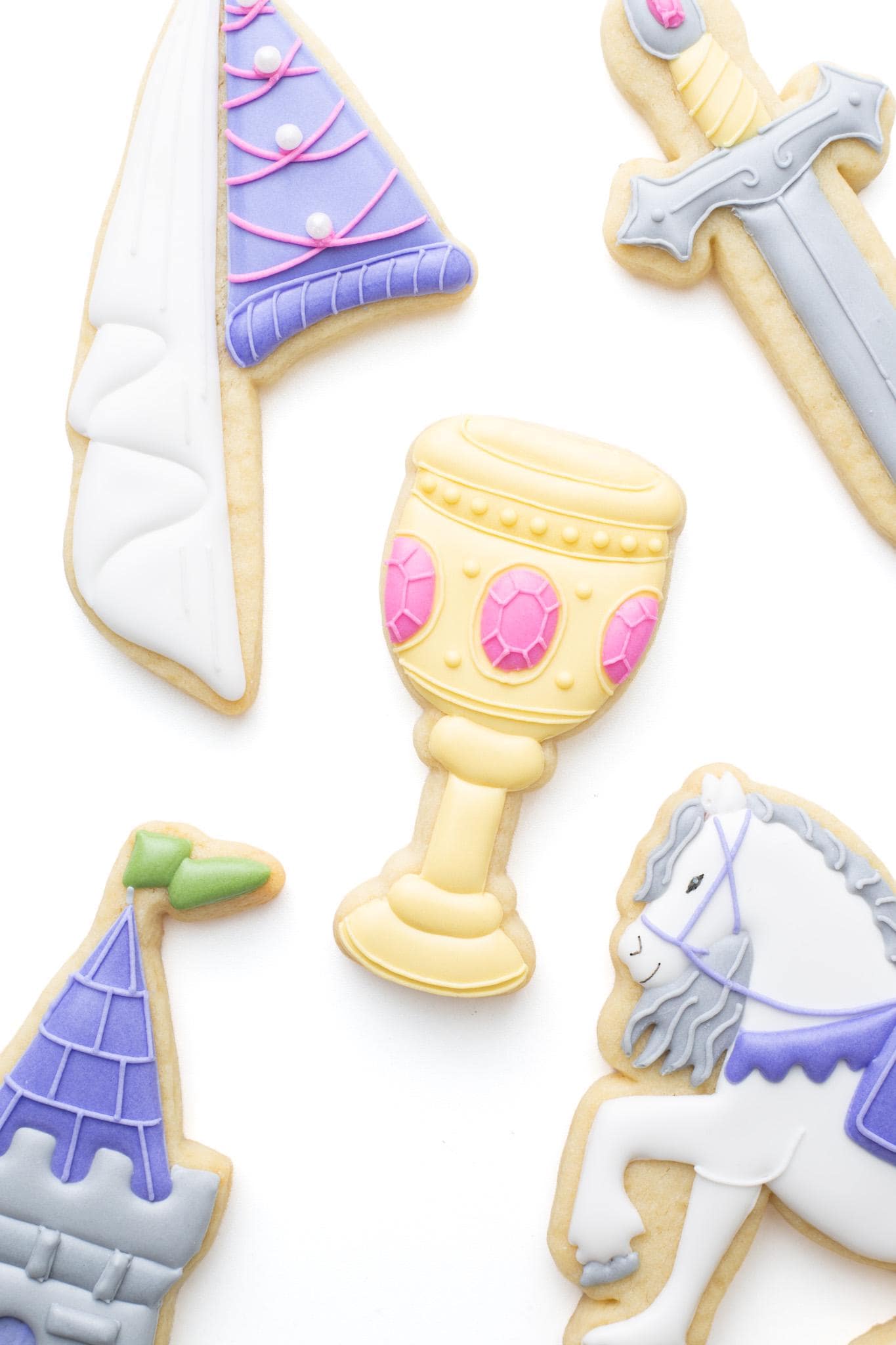 Goblet decorated sugar cookie next to medieval horse, castle tower, knight's sword, and princess hat.