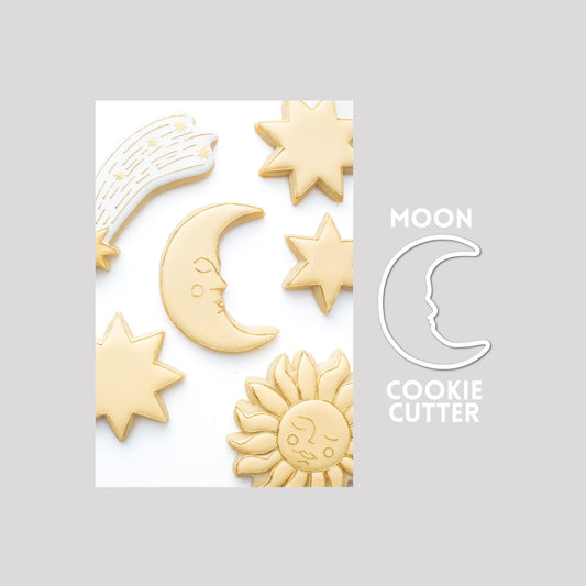 Decorated moon sugar cookie next to a moon cookie cutter outline on a gray background.