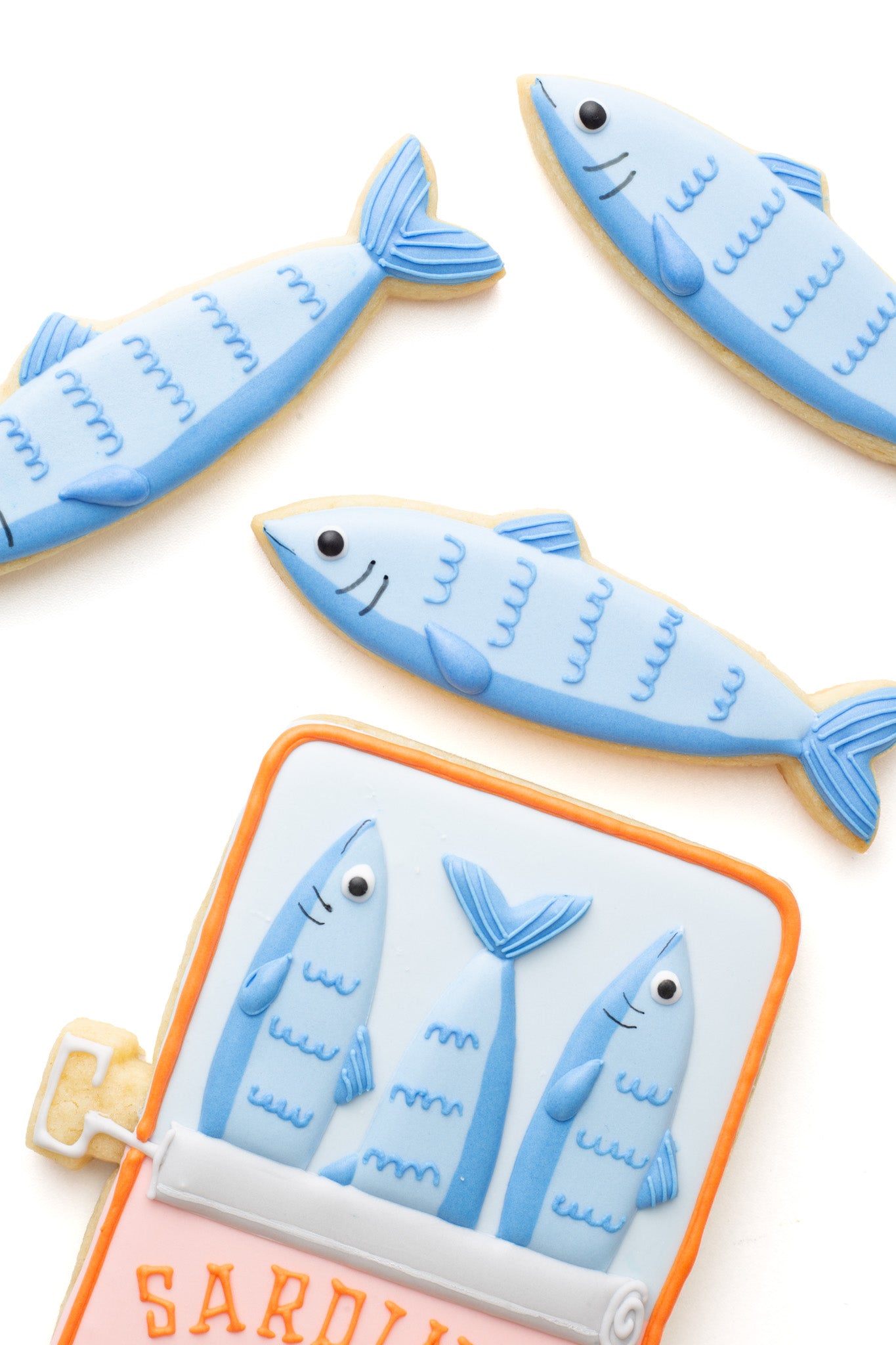 Decorated sardine fish sugar cookies next to a tins or cans of sardine fish.