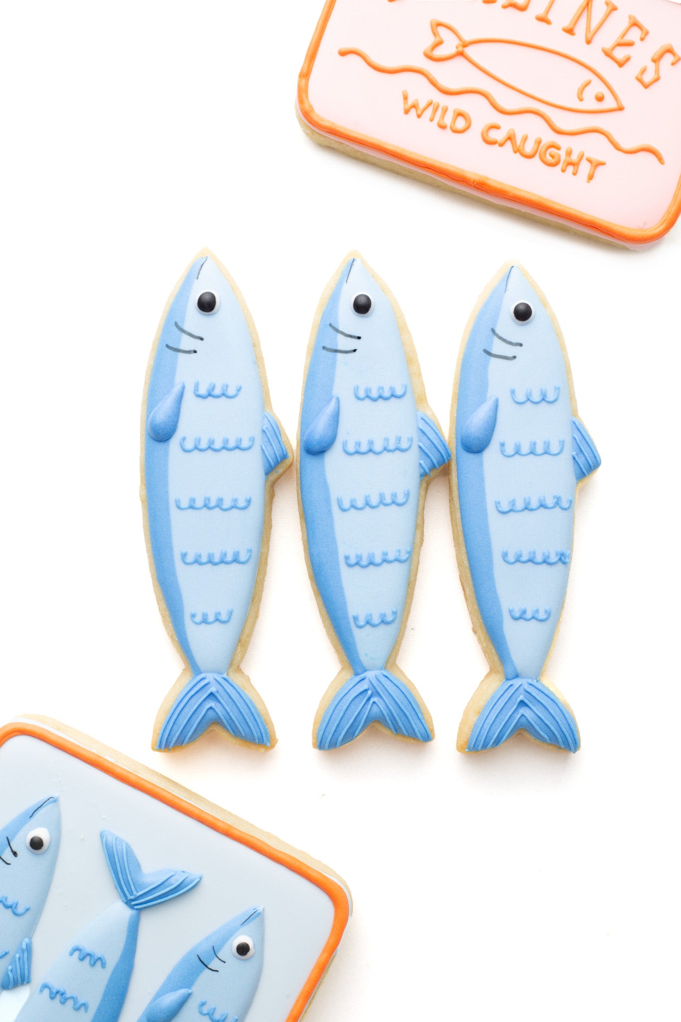 Decorated sardine fish sugar cookie next to a tins or cans of sardine fish.