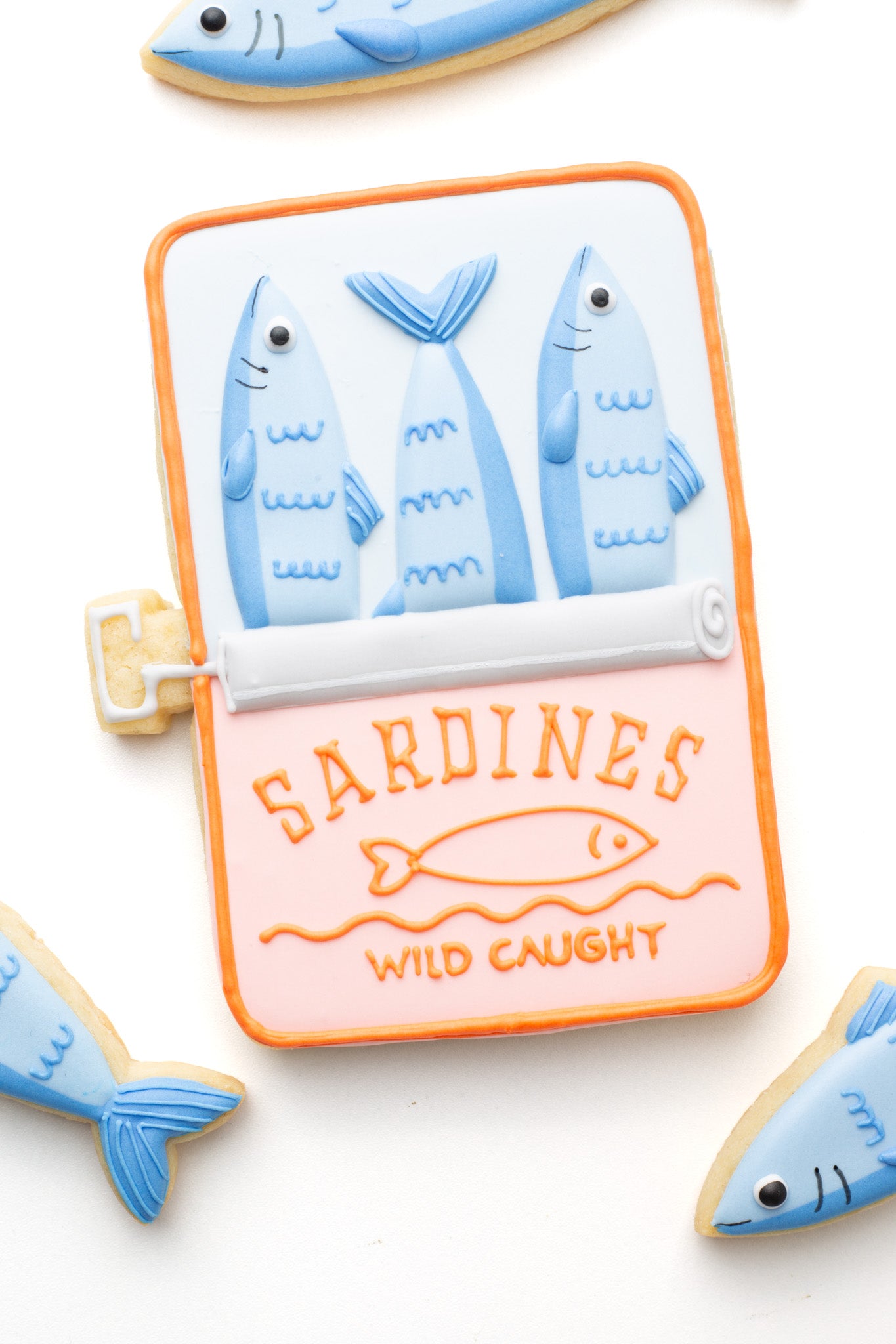 Decorated open tin or can of sardine fish sugar cookie next to sardine fish.