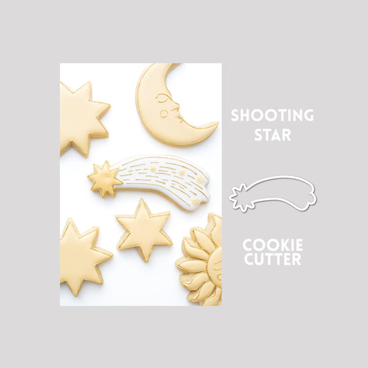Decorated shooting star sugar cookie next to a shooting star cookie cutter outline on a gray background.