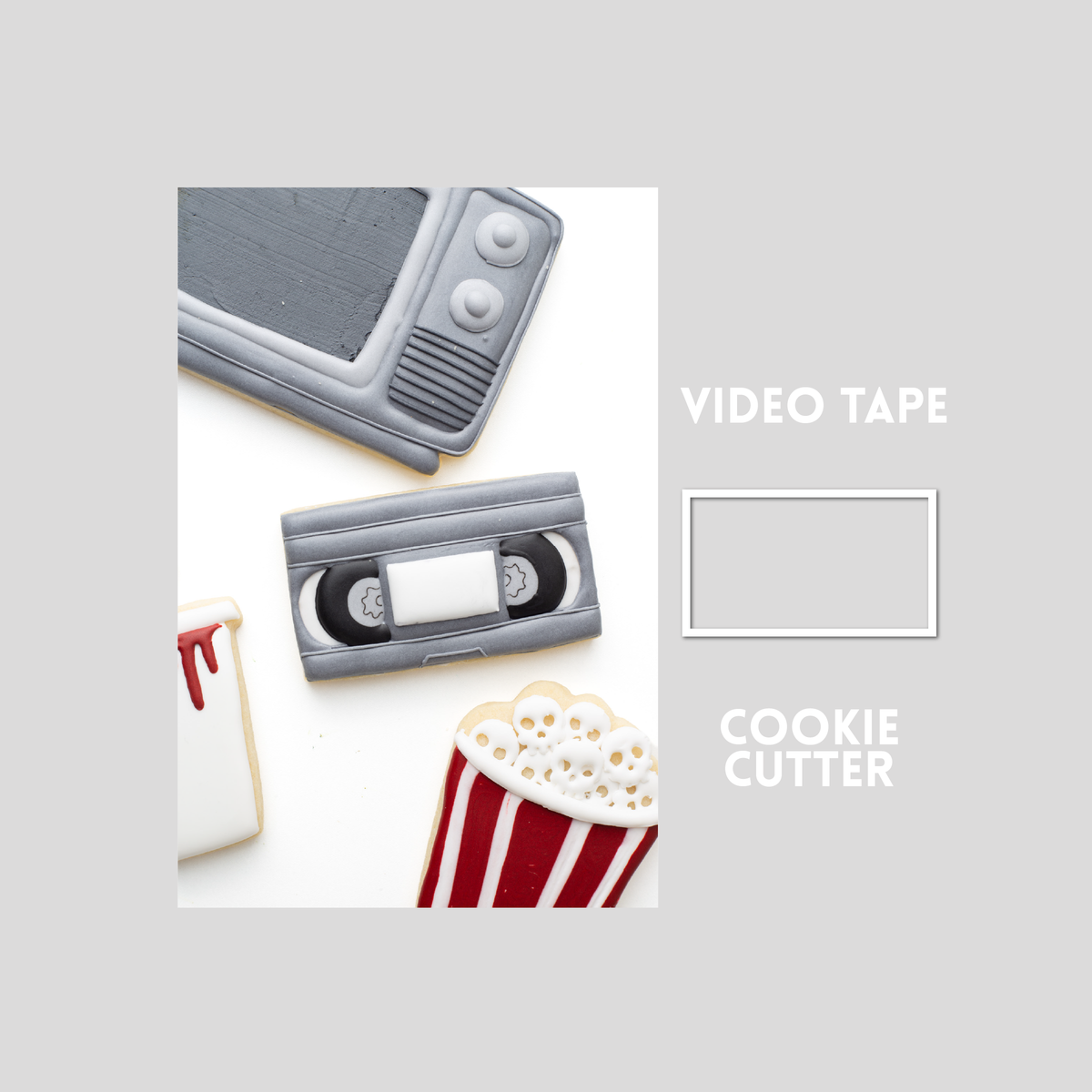 Decorated video tape sugar cookie next to a video tape cookie cutter outline on a gray background.