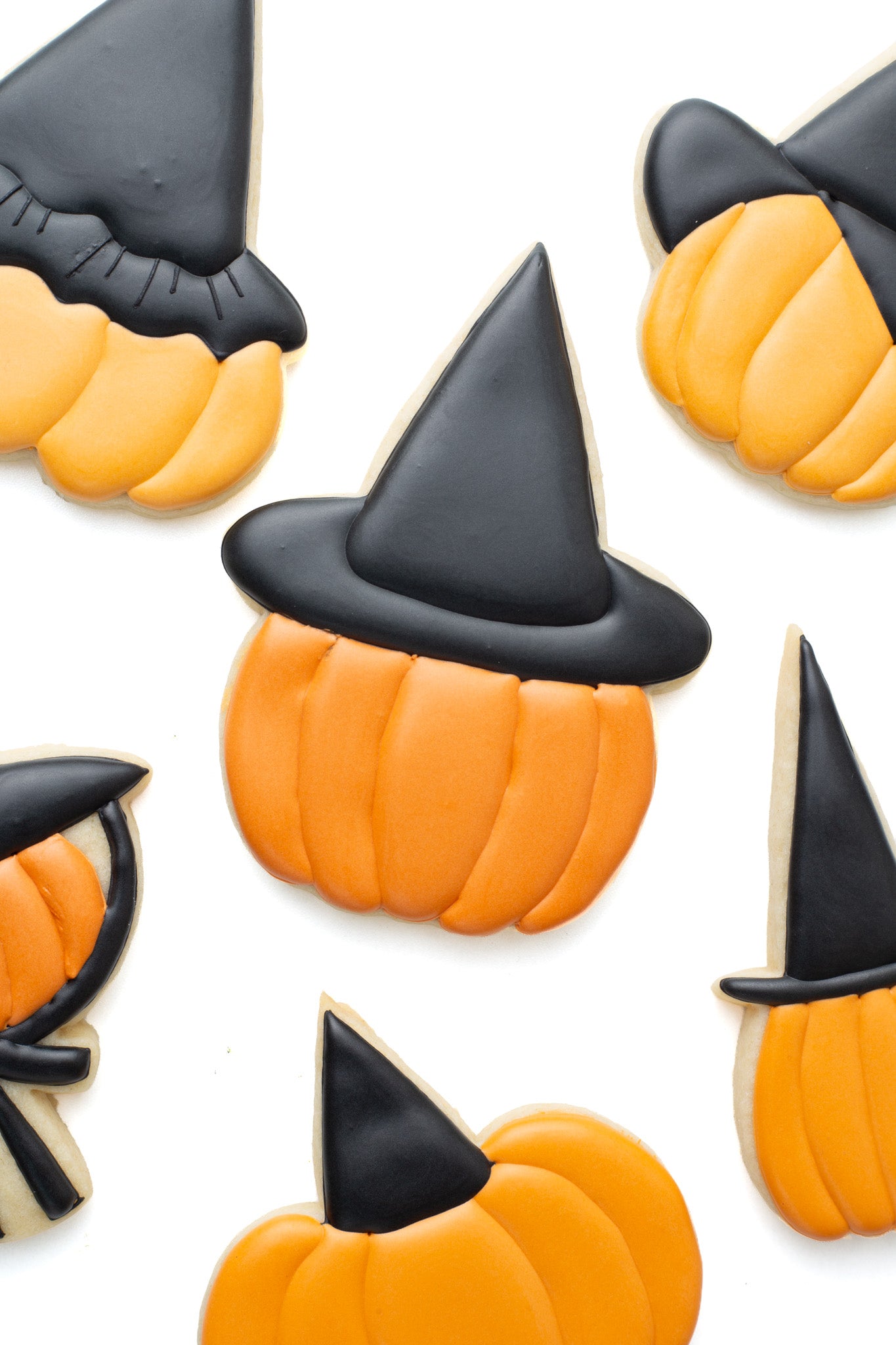 Pumpkin with witch hat decorated sugar cookie surrounded by various pumpkins with different witch hats on.