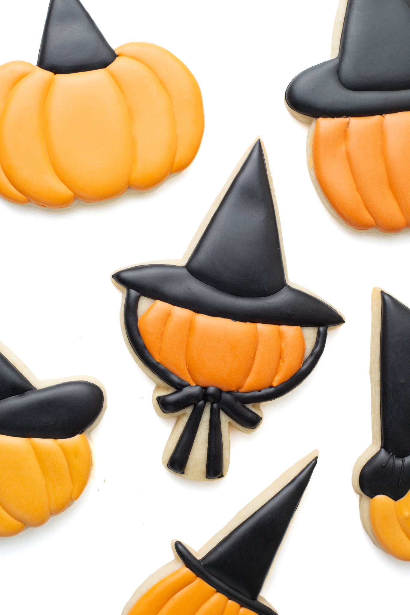 Pumpkin with witch hat with bow decorated sugar cookie surrounded by various pumpkins with different witch hats on.