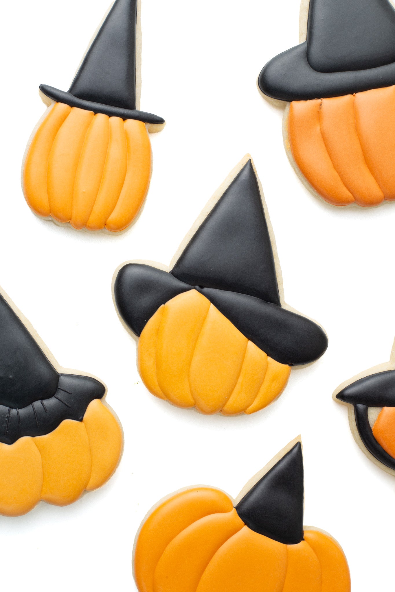 Pumpkin with witch hat decorated sugar cookie surrounded by various pumpkins with different witch hats on.