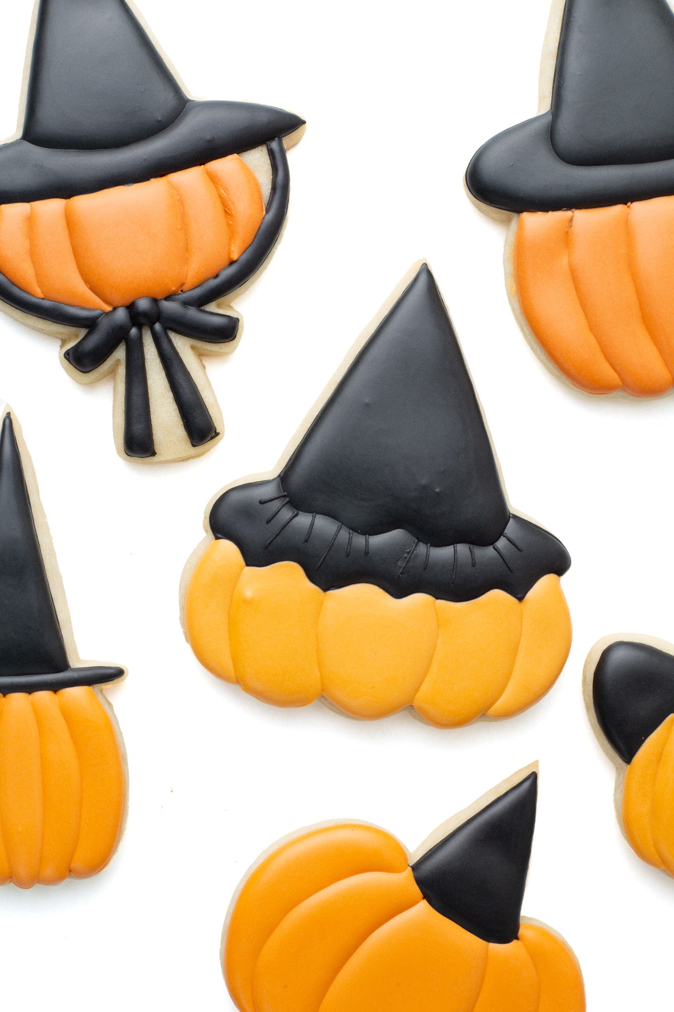 Pumpkin with witch hat decorated sugar cookie surrounded by various pumpkins with different witch hats on.