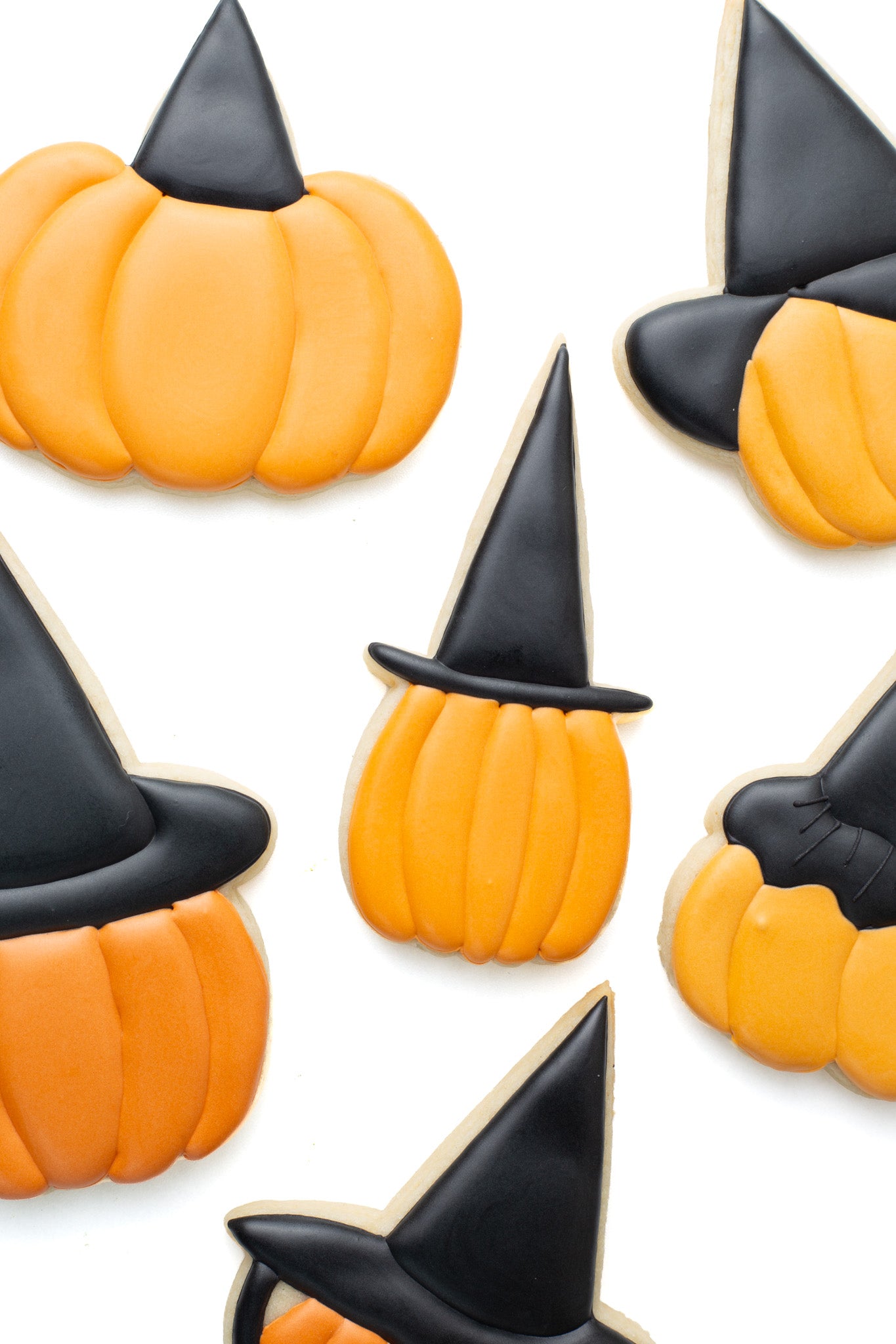 Pumpkin with tall witch hat decorated sugar cookie surrounded by various pumpkins with different witch hats on.