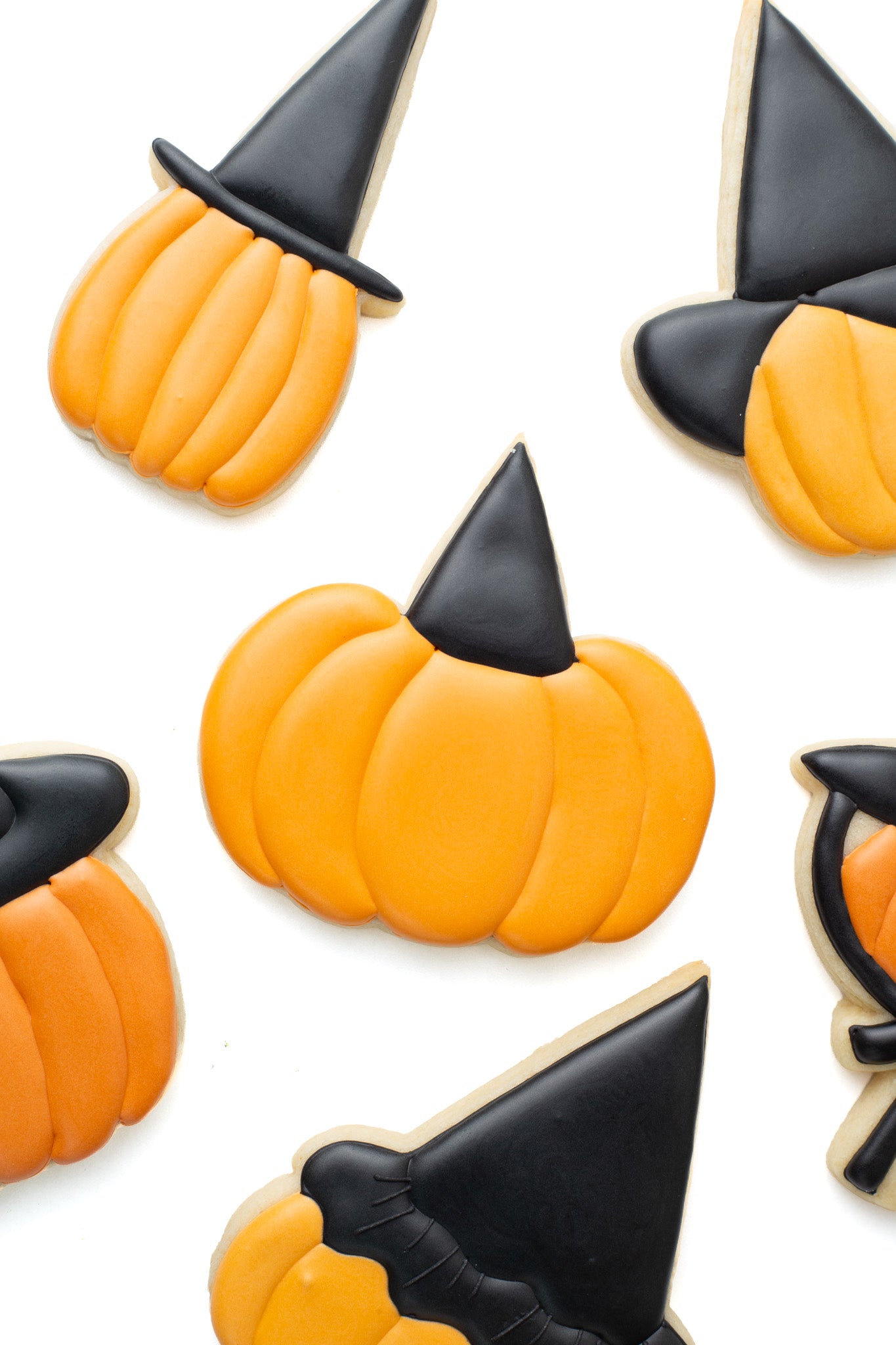 Pumpkin with witch hat decorated sugar cookie surrounded by various pumpkins with different witch hats on.