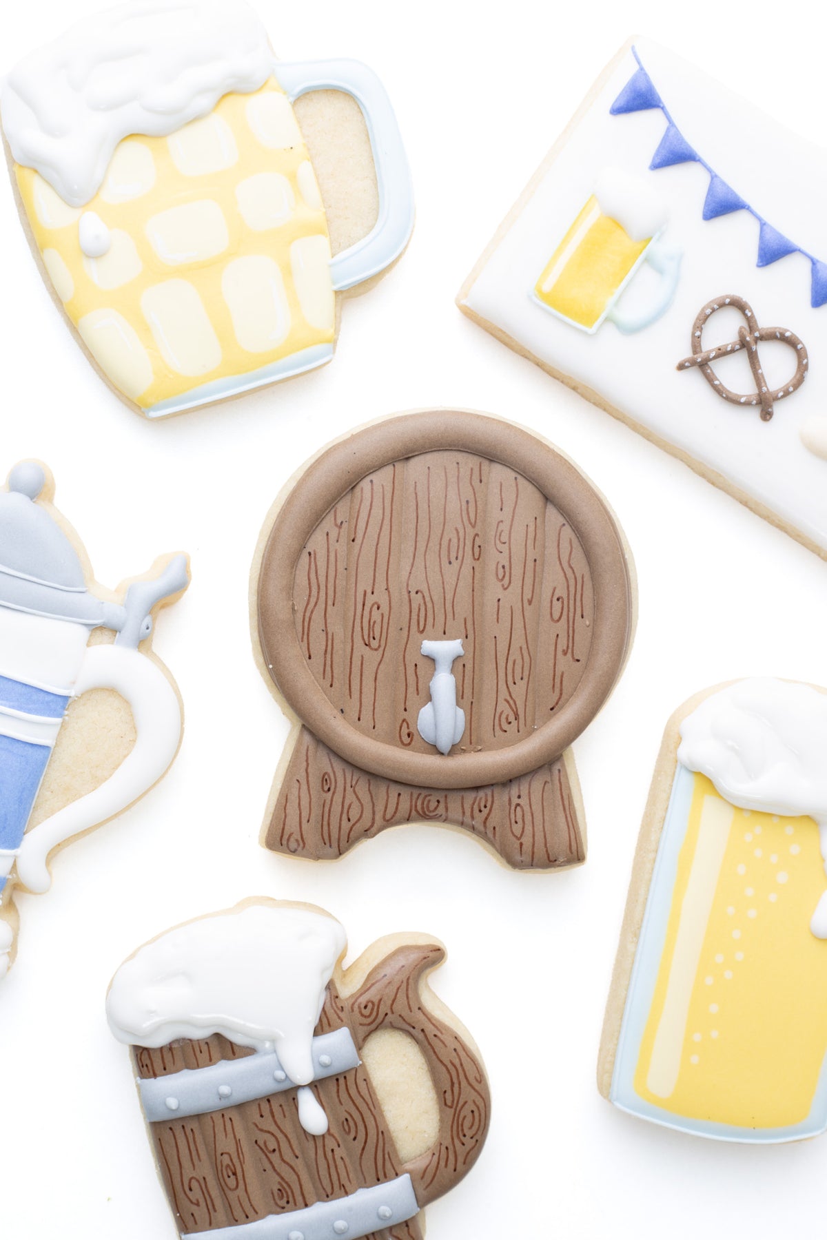 Oktoberfest themed cookies. A beer keg decorated sugar cookie next to a ,  beer stein, wood beer mug, beer mug, and dimple beer mug decorated sugar cookie.